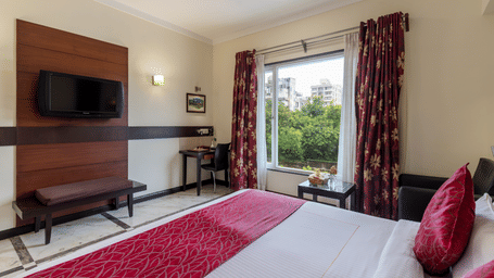 Interior of the Comfort Room showing a neatly made bed, wall-mounted television, and a large window filling the space with natural light - Amantra Comfort Hotel