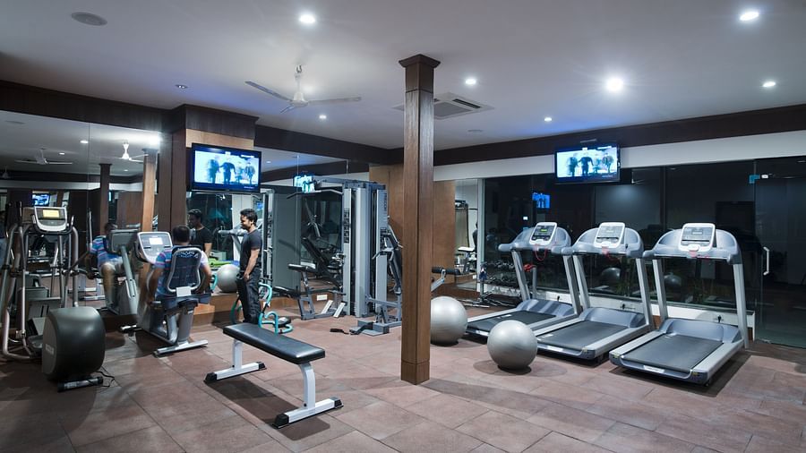 An image of a gym filled with various machines and equipment, showcasing a person standing while observing another individual engaged in a workout.