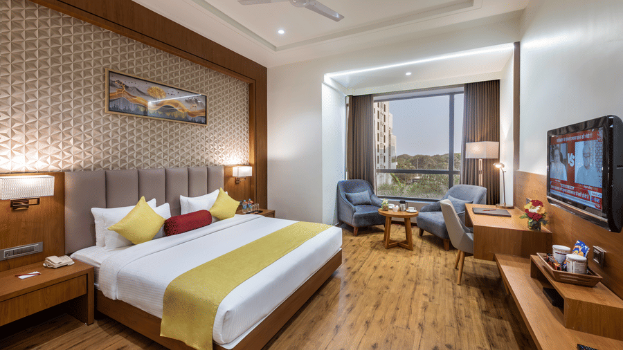 A premium room in Lords Inn Somnath with modern interiors, featuring a neatly made double bed and a large window offering a view of the outdoors.