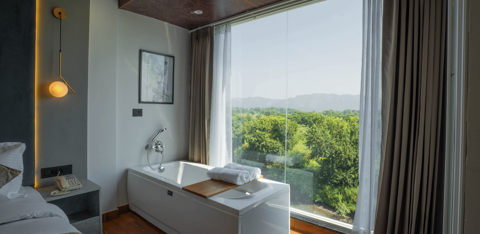 A guest room at Sukoon by the Ganges featuring a deep soaking tub right next to a window with lush green views.