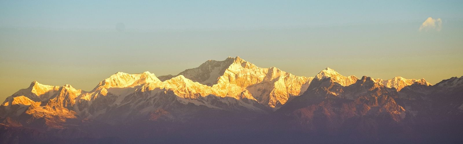 Snow-capped Himalayan mountain range glowing in golden sunlight under a clear blue sky, viewed from a scenic vantage point at sunrise.