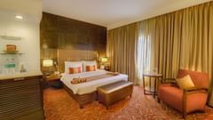 Premium Room at Pride Premier Chennai featuring a plush bed with a diwan at the foot and a couch placed next to the large window.