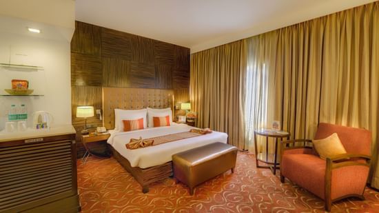 Premium Room at Pride Premier Chennai featuring a plush bed with a diwan at the foot and a couch placed next to the large window.