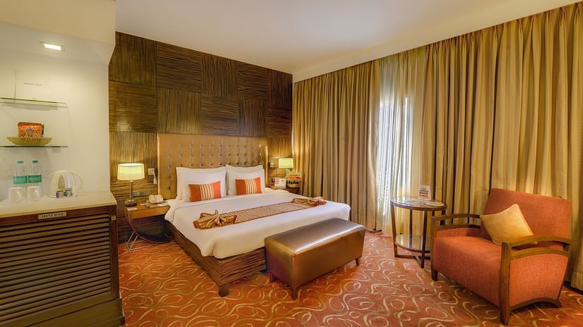 Premium Room at Pride Premier Chennai featuring a plush bed with a diwan at the foot and a couch placed next to the large window.