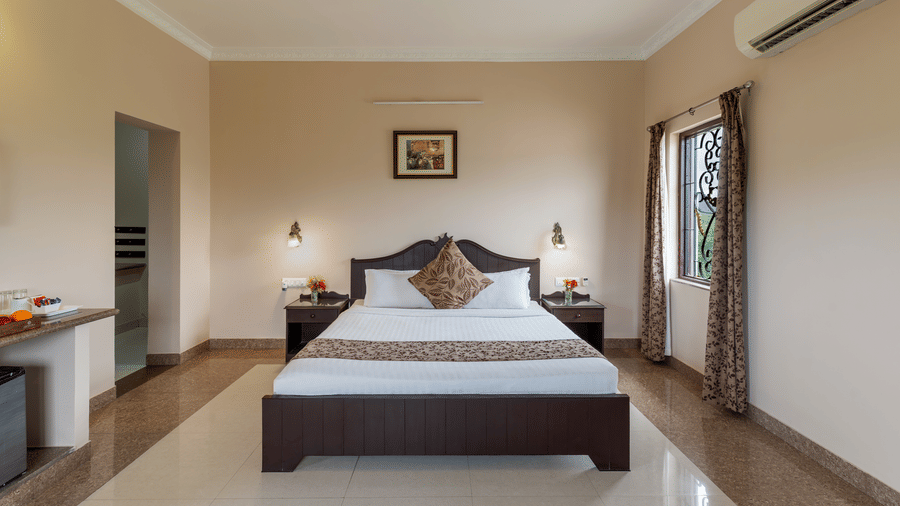 A spacious bedroom at Mewar Mansion Villa By Amantra, Udaipur features a dark wood double bed and air conditioning.