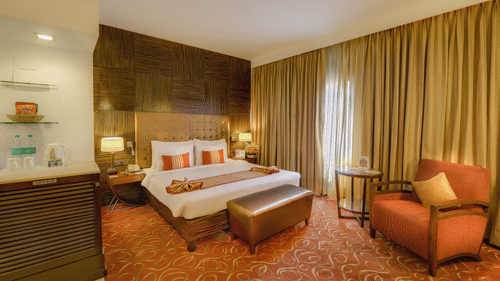 Premium Room at Pride Premier Chennai featuring a plush bed with a diwan at the foot and a couch placed next to the large window.