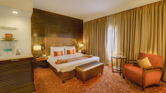 Premium Room at Pride Premier Chennai featuring a plush bed with a diwan at the foot and a couch placed next to the large window.