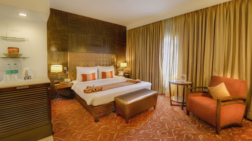 Premium Room at Pride Premier Chennai featuring a plush bed with a diwan at the foot and a couch placed next to the large window.