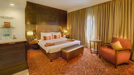 Premium Room at Pride Hotel Chennai featuring a plush bed with a diwan at the foot and a couch placed next to the large window