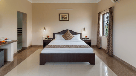 A spacious bedroom at Mewar Mansion Villa By Amantra, Udaipur features a dark wood double bed and air conditioning.