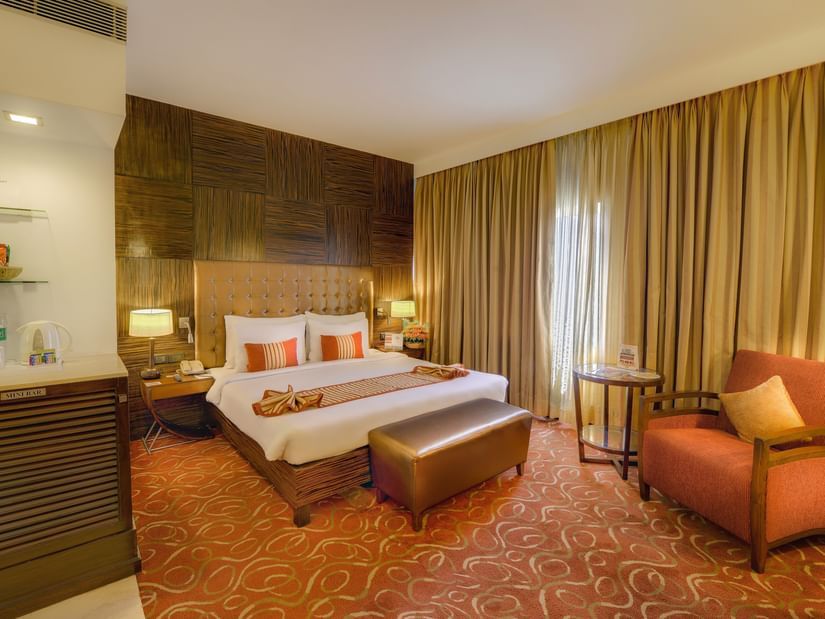 Premium Room at Pride Premier Chennai featuring a plush bed with a diwan at the foot and a couch placed next to the large window.