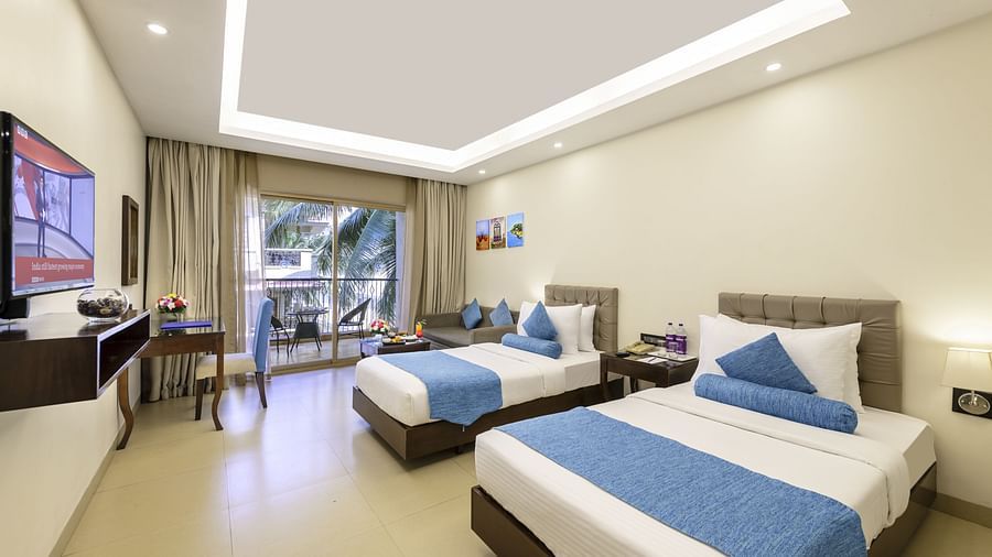 a twin bedroom in candolim featuring two single cots, a wall-mounted television, a work desk and a balcony that opens to verdant views - Golden Tulip, Candolim, Goa