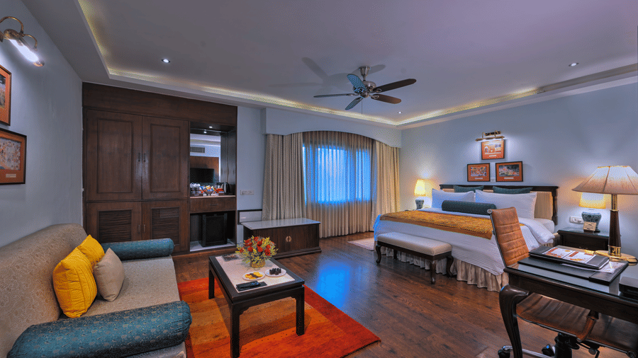A room with a large bed, spreads, pillows, chairs, sofa, a table, and windows. | Clarks Varanasi