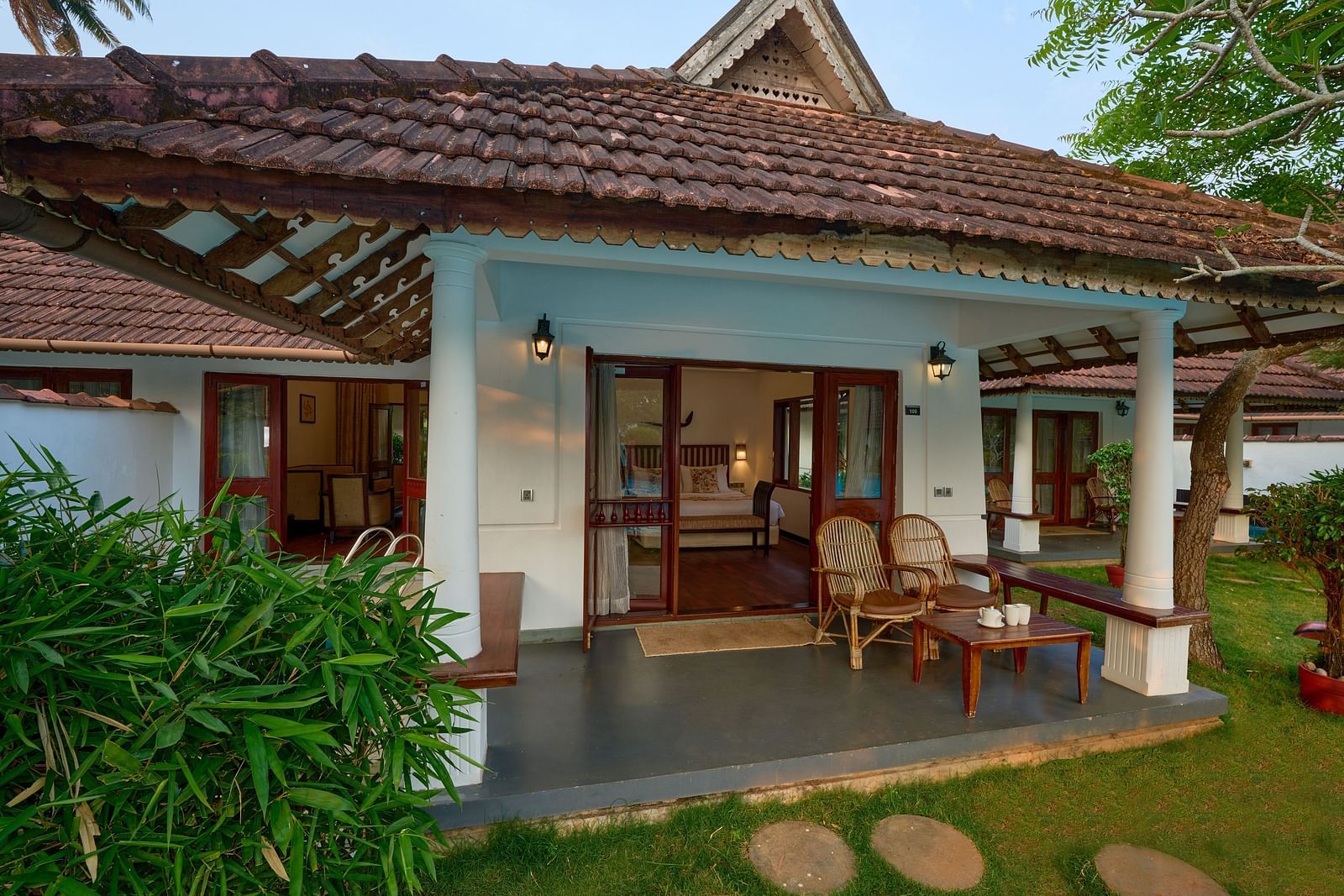 an image of a veranda with two wooden finished chairs and a table - Rhythm Kumarakom
