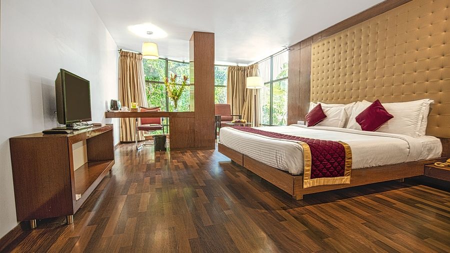 A photo of a hotel room with a king size bed, a TV, a desk, and a large window.