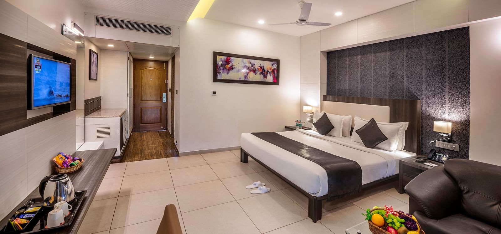 A well-appointed hotel room, featuring a bed, seating area with a couch, a refreshment centre, and a wall-mounted television.