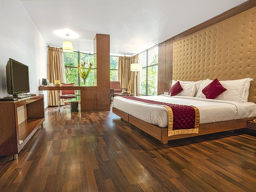 A photo of a hotel room with a king size bed, a TV, a desk, and a large window.