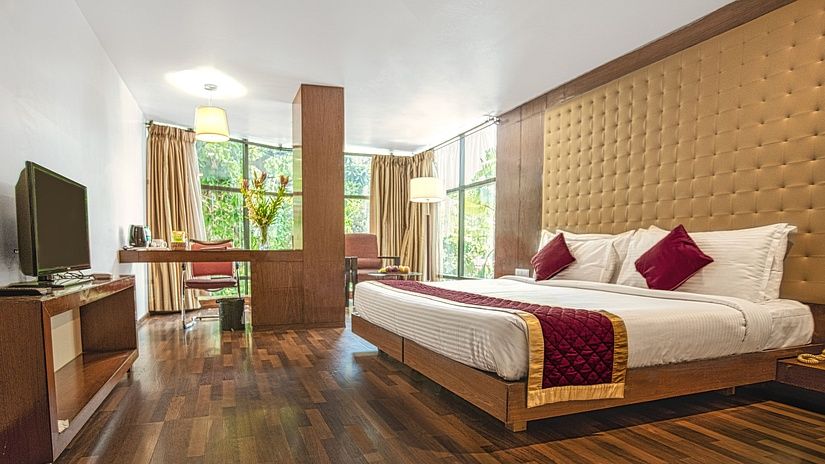 A photo of a hotel room with a king size bed, a TV, a desk, and a large window.