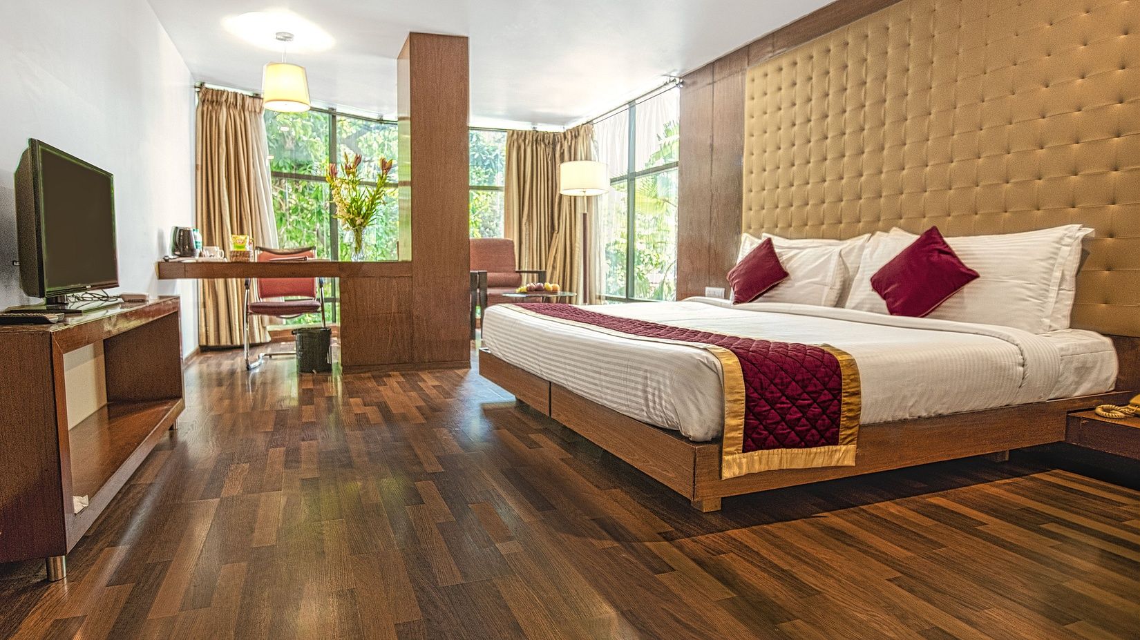 A photo of a hotel room with a king size bed, a TV, a desk, and a large window.