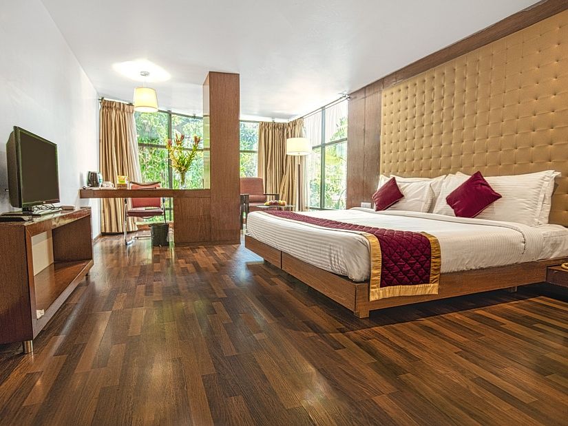 A photo of a hotel room with a king size bed, a TV, a desk, and a large window.