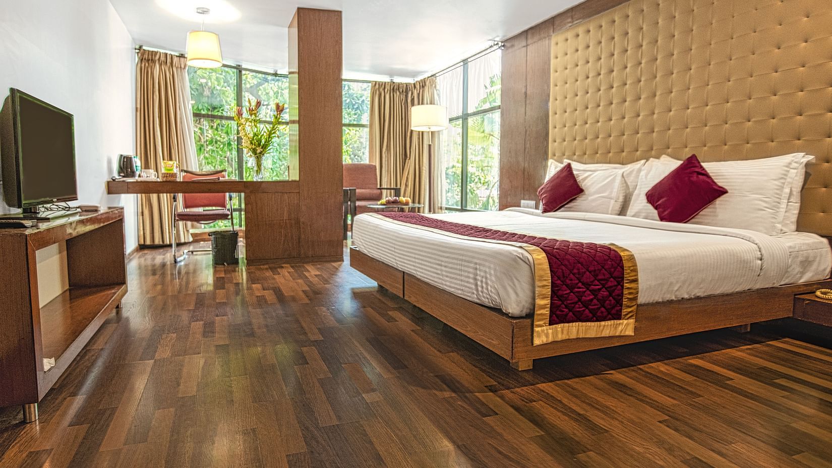 A photo of a hotel room with a king size bed, a TV, a desk, and a large window.