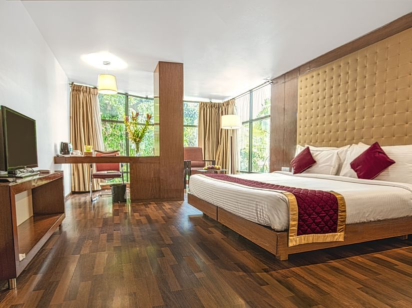 A photo of a hotel room with a king size bed, a TV, a desk, and a large window.