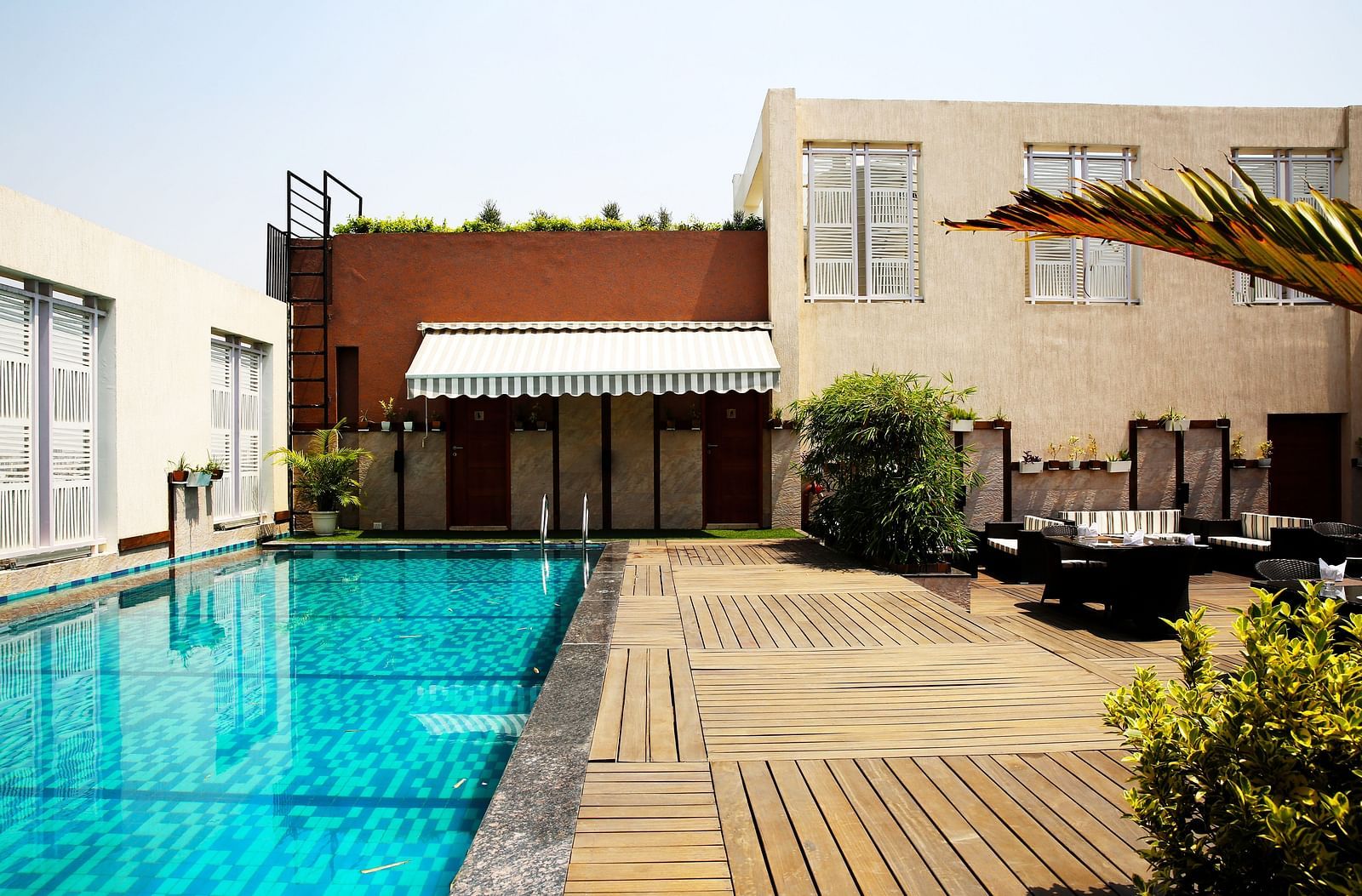 A swimming pool with wooden deck besides it and am open air common seating area in the corner - Ramada by Wyndham, Ghaziabad, Vasundhara