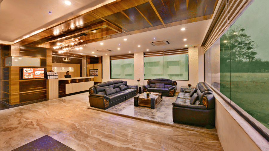 The interior of a well-lit hotel lobby, at Lords Inn Porbandar, features comfortable seating, wooden accents, and a welcoming atmosphere.