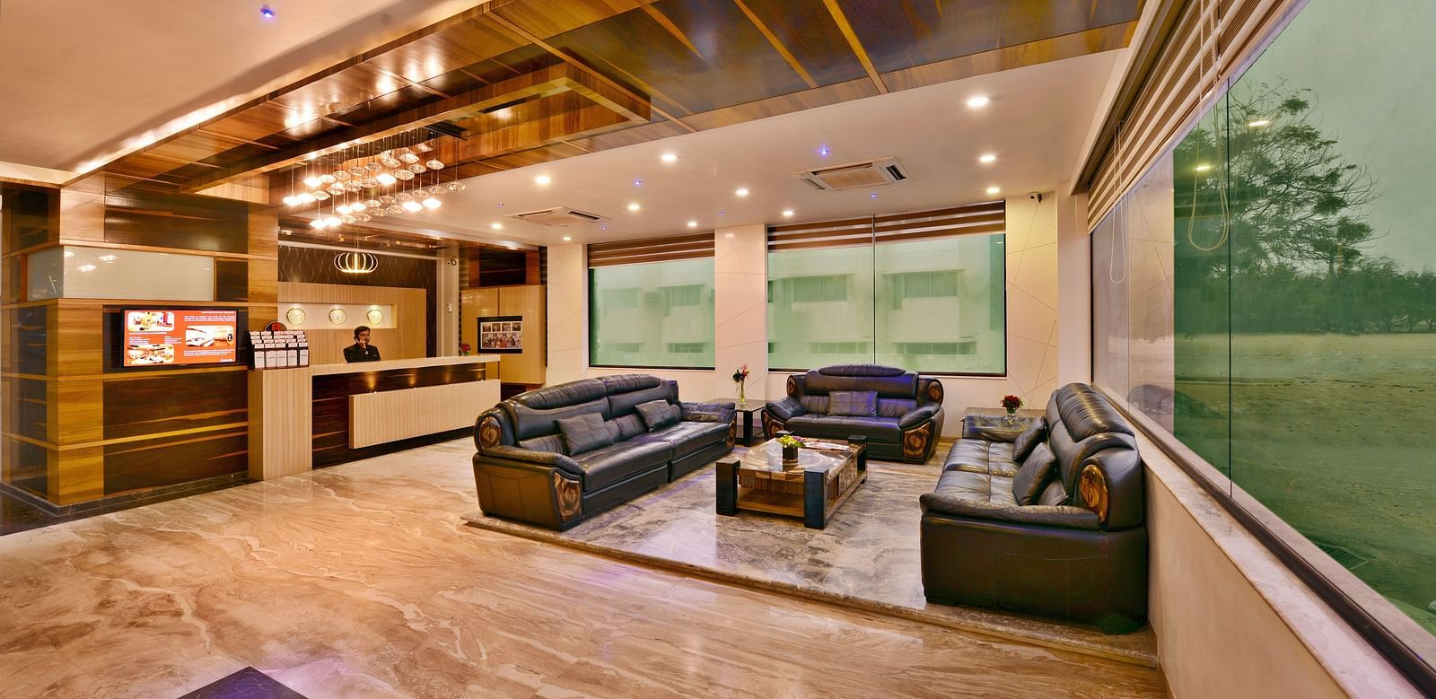 The interior of a well-lit hotel lobby, at Lords Inn Porbandar, features comfortable seating, wooden accents, and a welcoming atmosphere.