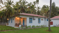A white resort cottage with a red roof and blue window frames, surrounded by palm trees and green lawns - Ibex Resorts, Coimbatore (Kakarla)