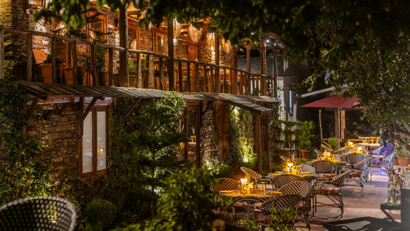 Evening terrace dining at The Manor Wellness & Sports Hotel - rustic stone architecture with warm lighting & intimate wicker seating among lush greenery.