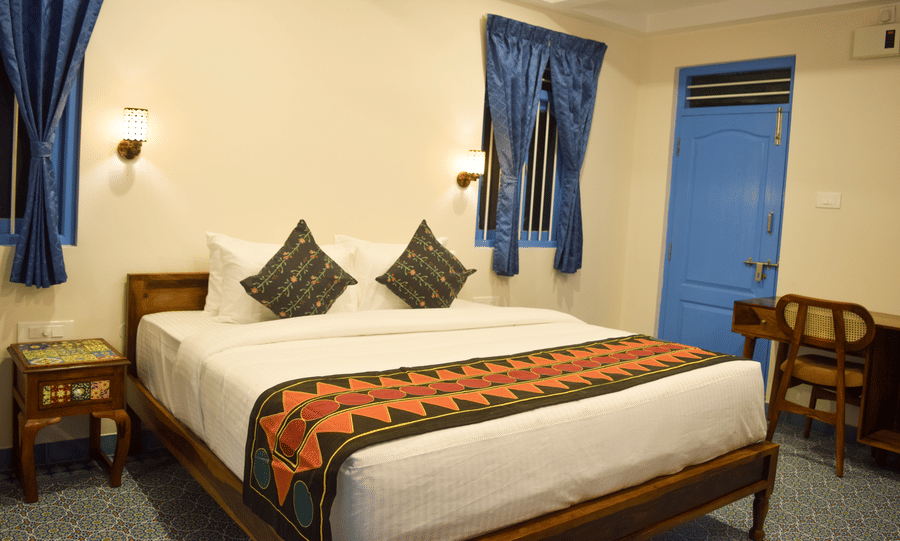 A hotel room with a double bed, blue accents, and traditional Indian textile patterns - Ibex Resorts, Coimbatore (Kakarla)