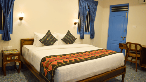 A hotel room with a double bed, blue accents, and traditional Indian textile patterns - Ibex Resorts, Coimbatore (Kakarla)
