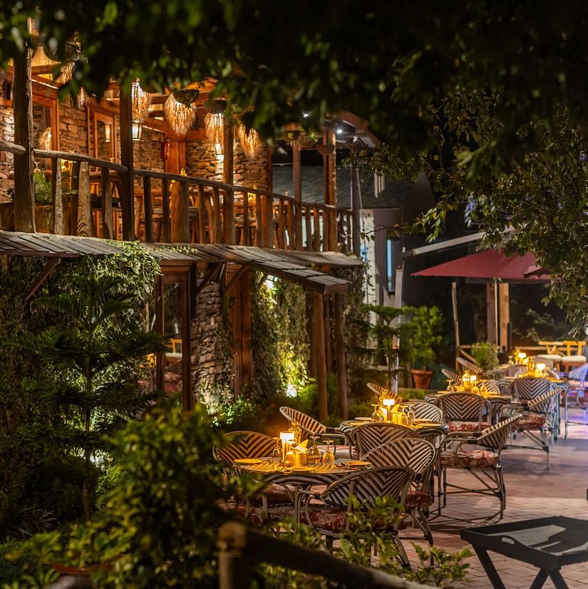 Evening terrace dining at The Manor Wellness & Sports Hotel - rustic stone architecture with warm lighting & intimate wicker seating among lush greenery.