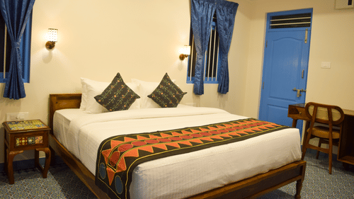 A hotel room with a double bed, blue accents, and traditional Indian textile patterns - Ibex Resorts, Coimbatore (Kakarla)