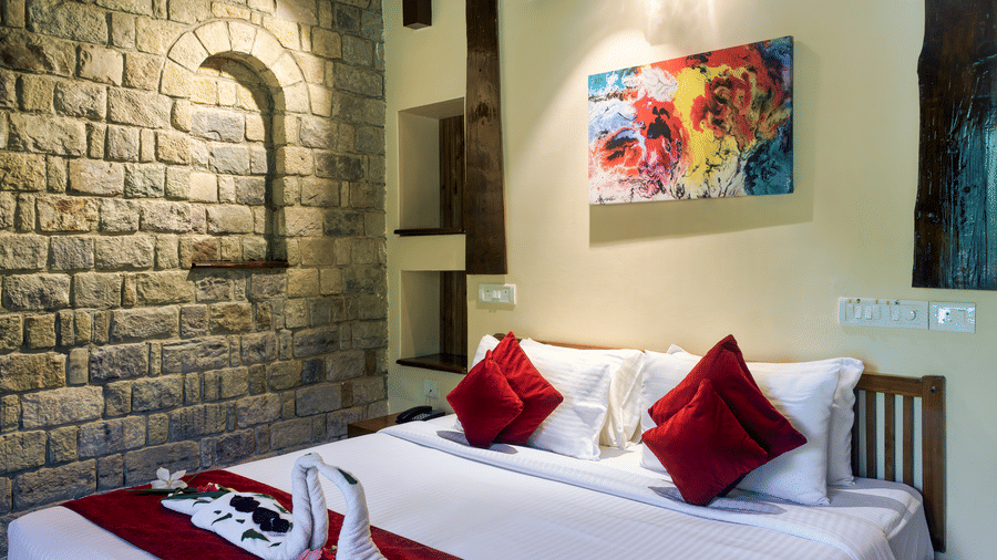 Comfortable guest room at Infinity Resorts Corbett featuring a double bed with decorative towel art, a stone accent wall, bedside lighting, and contemporary artwork.