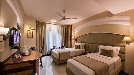 Hotel room with a bed, a TV, a nightstand, and a ceiling fan, captured with a wide-angle view - Lords Inn Vadodara
