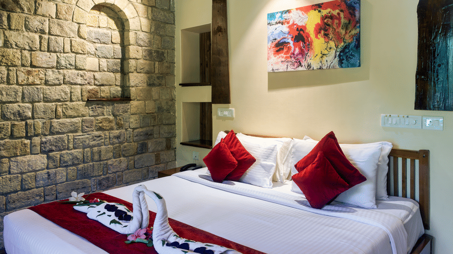 Comfortable guest room at Infinity Resorts Corbett featuring a double bed with decorative towel art, a stone accent wall, bedside lighting, and contemporary artwork.