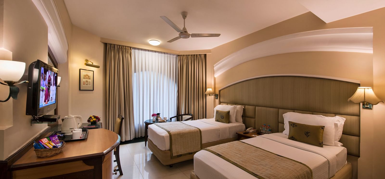 Hotel room with a bed, a TV, a nightstand, and a ceiling fan, captured with a wide-angle view - Lords Inn Vadodara