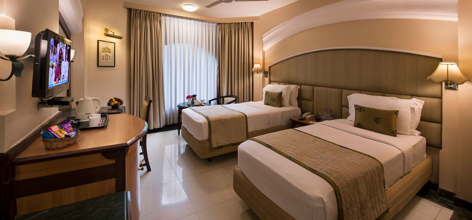 Hotel room with a bed, a TV, a nightstand, and a ceiling fan, captured with a wide-angle view - Lords Inn Vadodara