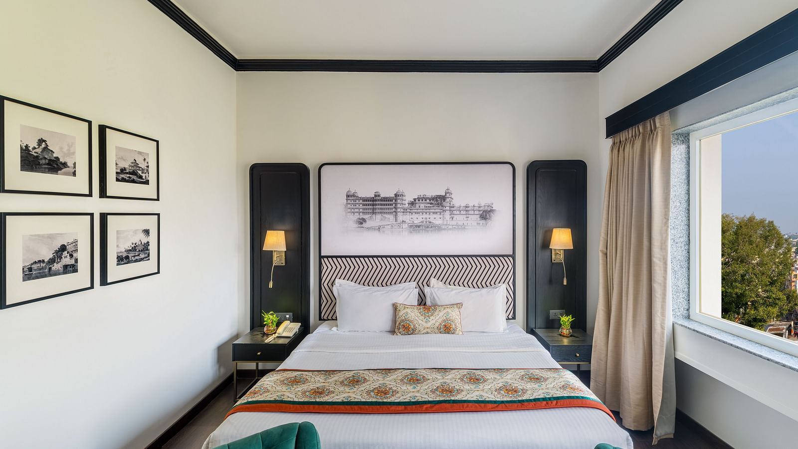 a king size bed with a window on the side and wall decor all around - Hotel Rajdarshan, Udaipur.