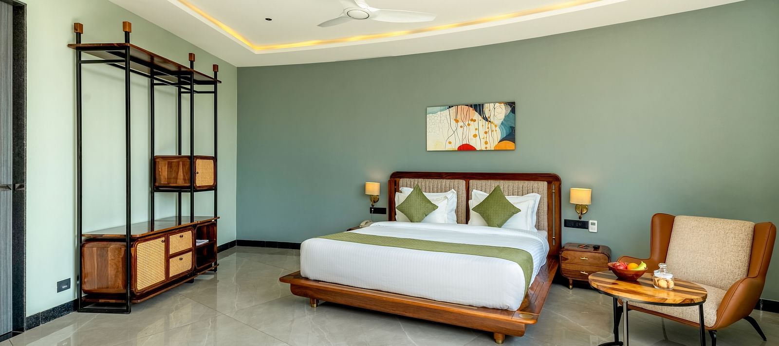 Pool View Room featuring a king size bed with a green and white patterned bedspread, wooden furniture, and a large window with sheer curtains at The Qualia Resort Club & Brewery, Udaipur.