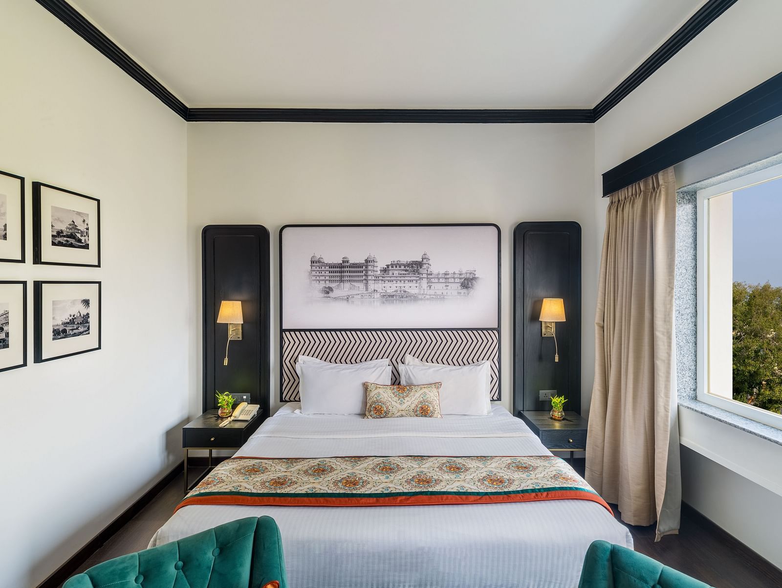 a king size bed with a window on the side and wall decor all around - Hotel Rajdarshan, Udaipur.