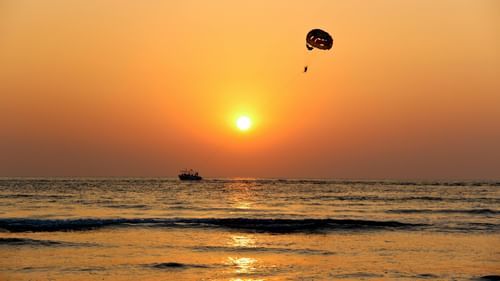 A person paragliding on the open sea at sunset