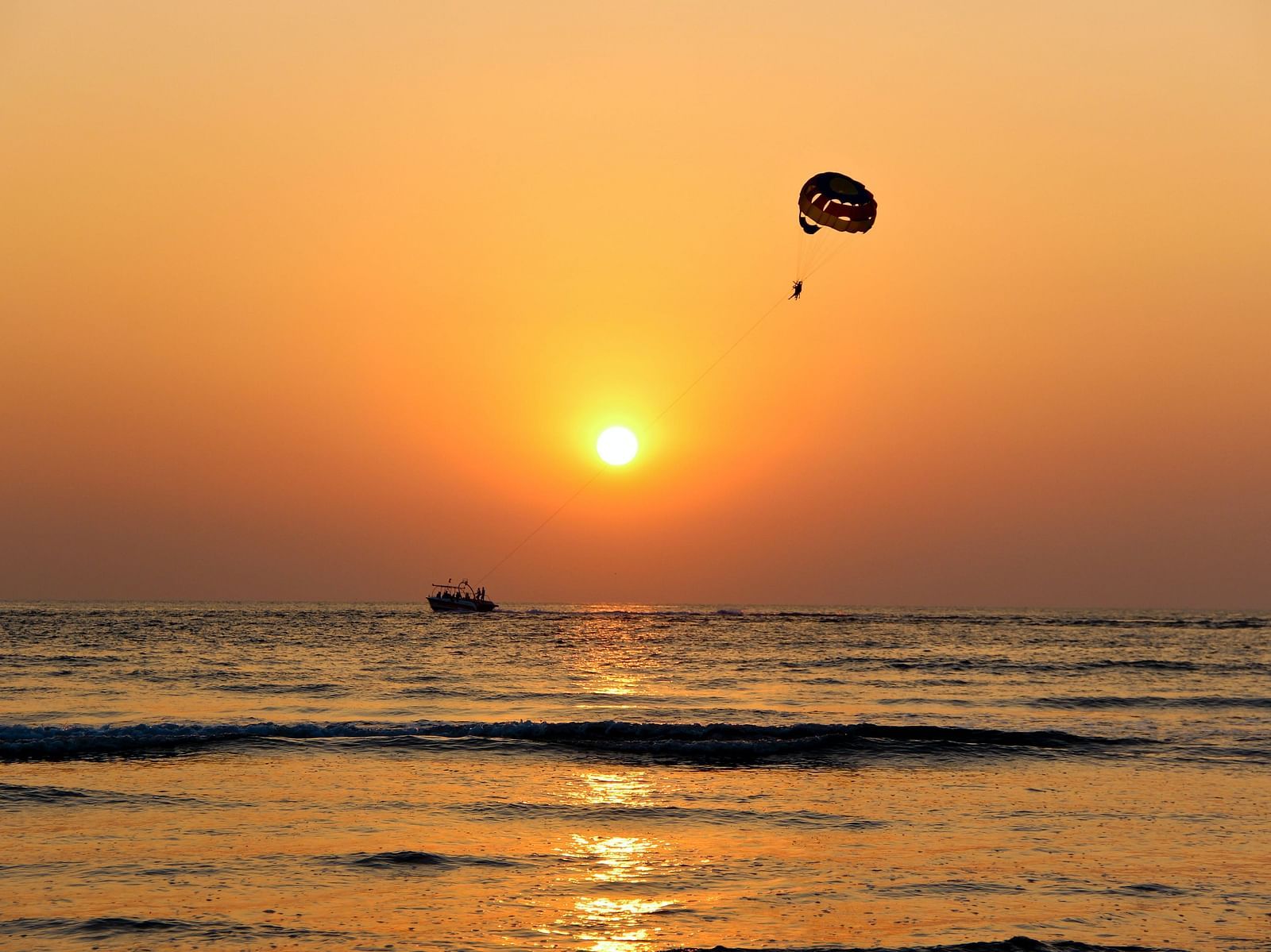 Prachute flying above  a beach at sunset