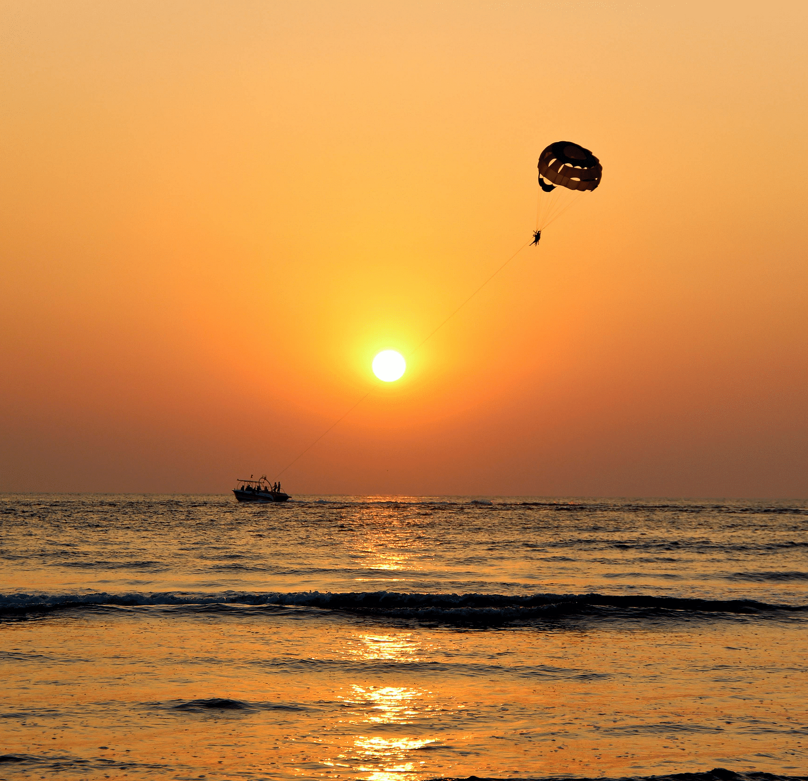 A view during the sunset at the beach of a person parasailing.