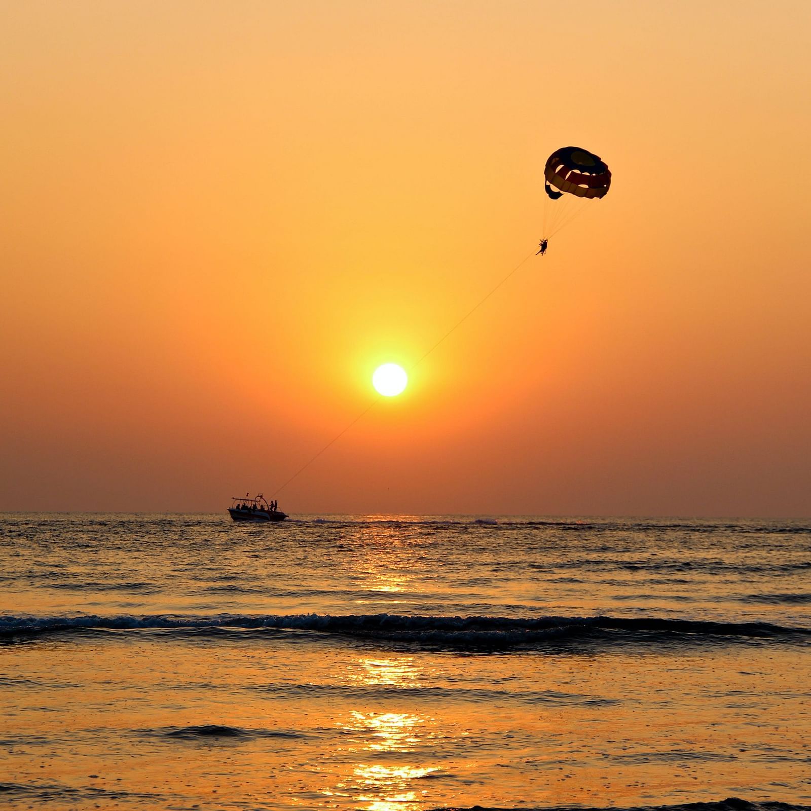 Prachute flying above  a beach at sunset