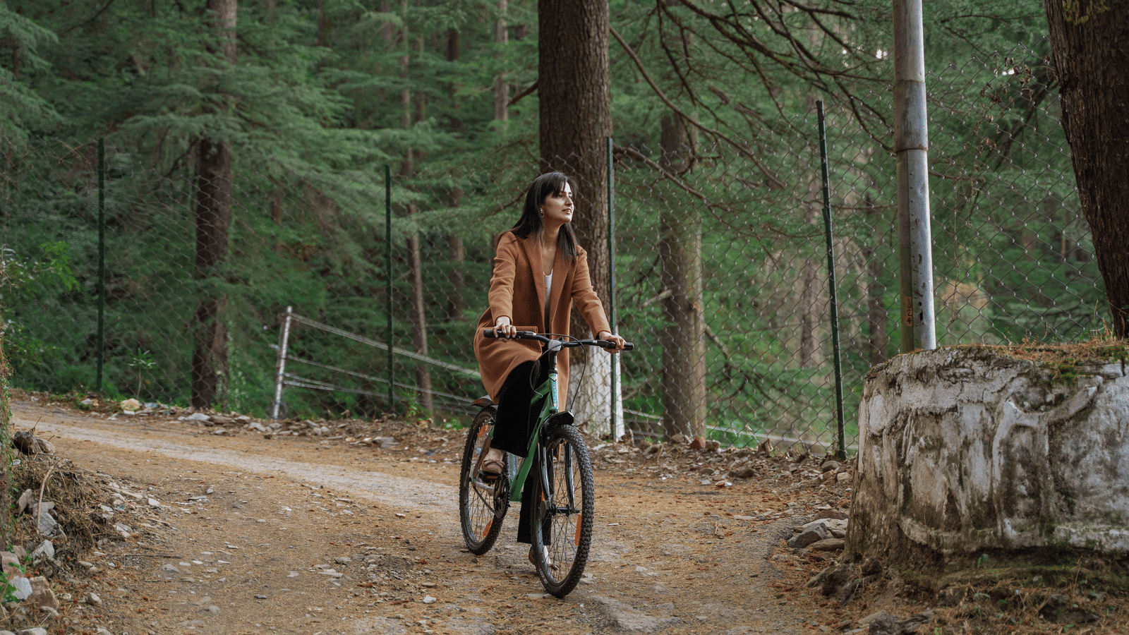 A woman riding a bicycle on a forest trail surrounded by tall trees, near Perfectstayz Value Shimla (Namah Retreat).