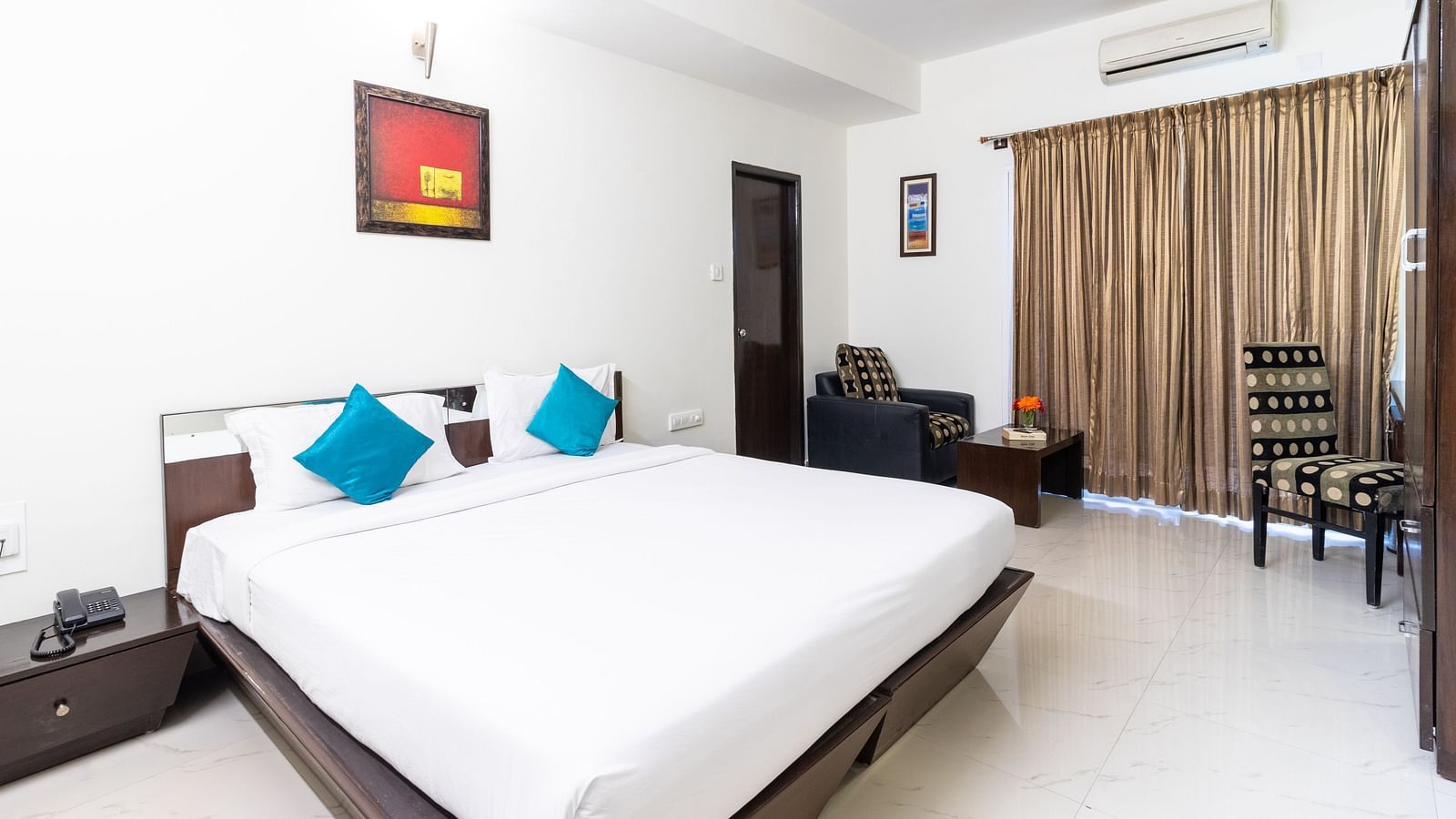 A room featuring a double bed with blue cushions and dark wooden furniture at Sanctum Suites Domlur, Bangalore.