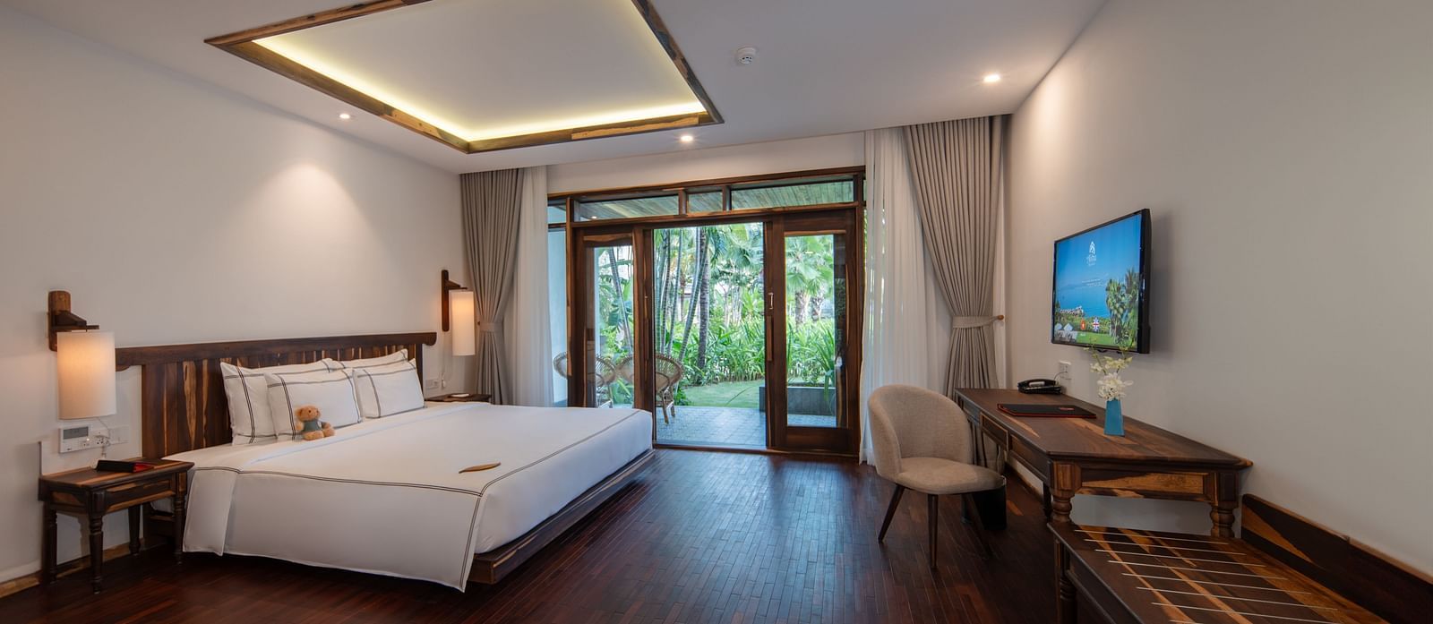 A bedroom with a plush bed, ambient lighting and a glassdoor opening up to a garden - Alibu Resort Nha Trang